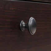 A close-up of a dark brown wooden cabinet or dresser drawer featuring a round, dark metal knob with a textured, matte finish.