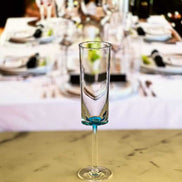 One unbreakable blue acrylic champagne flute from the set of 4, placed in front of a festive dining table setup.