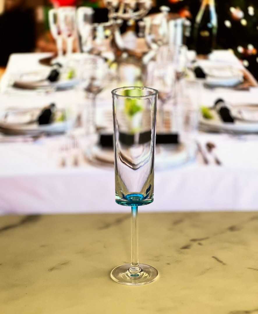 One unbreakable blue acrylic champagne flute from the set of 4, placed in front of a festive dining table setup.