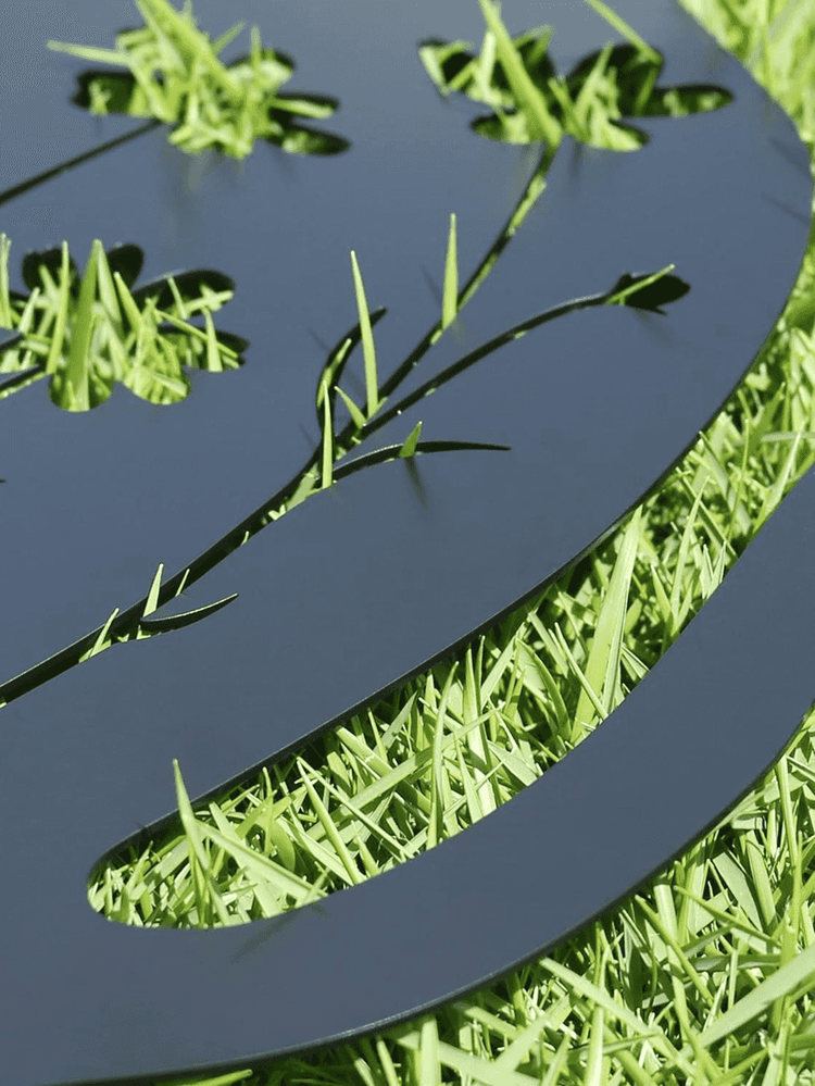 Metallic decorative object with cut-out grass design on a grassy background