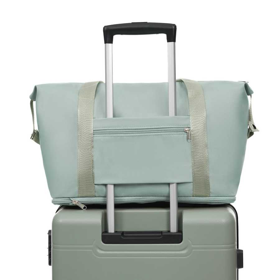 Light green duffel bag with beige straps on top of a green suitcase with a white background