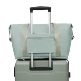 Light green duffel bag with beige straps on top of a green suitcase with a white background
