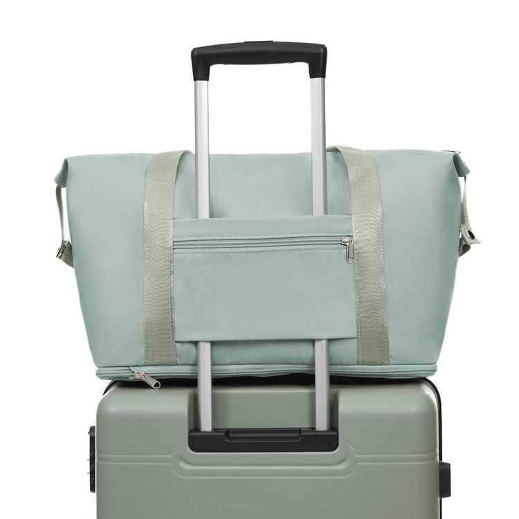 Light green duffel bag with beige straps on top of a green suitcase with a white background