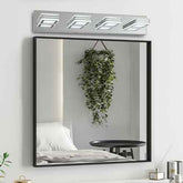 Large rectangular mirror with black frame on a white wall, illuminated by a modern light fixture.