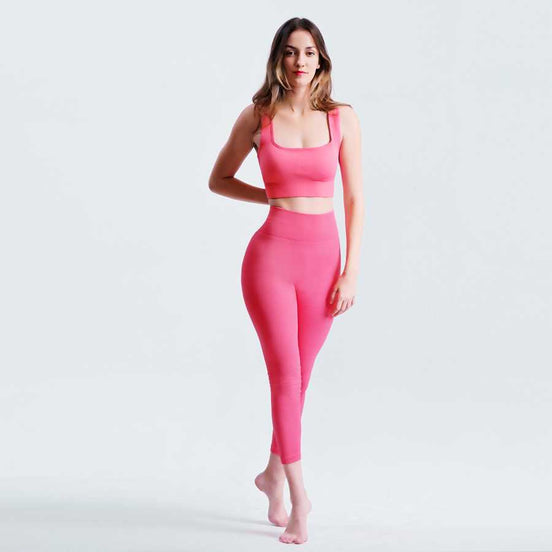 Woman wearing a pink sports bra and leggings on a light gray background