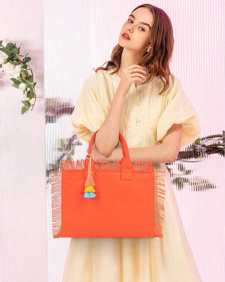 Woman holding an orange tote bag with tassels against a light pink background