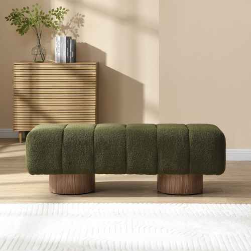 Green textured bench with wooden legs in a room with a beige wall and wooden floor.