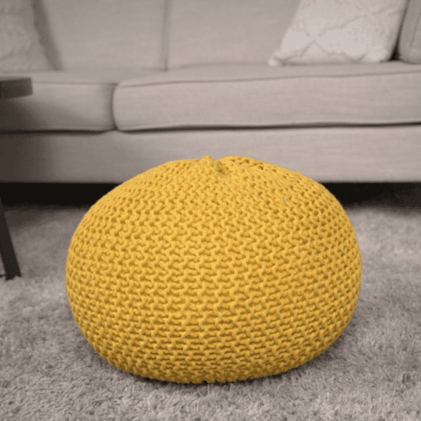 Yellow knitted pouf on a gray carpet with a gray sofa in the background