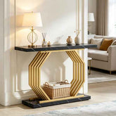 A modern console table with a black marble top and base, and a geometric gold metal frame, styled in a bright living room with a lamp, vases, and a basket underneath.