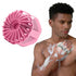 Man using a pink scrubber on his arm with a close-up of the scrubber on a white background.