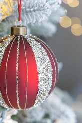 Red Christmas ornament with silver glitter on a blurred Christmas tree background