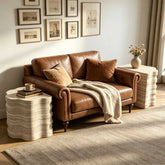 Living room with beige sofa, framed artwork, textured side table with a vase, books, and a cozy blanket