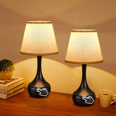 Two black table lamps with beige lampshades on a wooden surface.