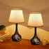 Two black table lamps with beige lampshades on a wooden surface.