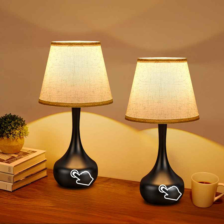 Two black table lamps with beige lampshades on a wooden surface.
