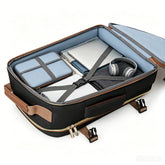 An open black and brown soft-sided suitcase or laptop bag with a light blue interior, shown holding a laptop, a blue padded case, and over-ear headphones on a clean white background.