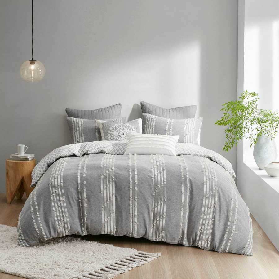Gray patterned comforter on a bed in a modern bedroom with a plant and side table.