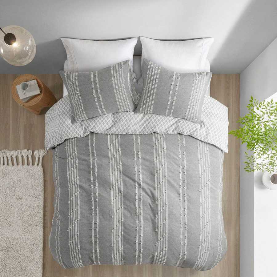 Gray and white striped bedding set on a bed with pillows and a lamp in the background.