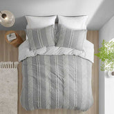 Gray and white striped bedding set on a bed with pillows and a lamp in the background.