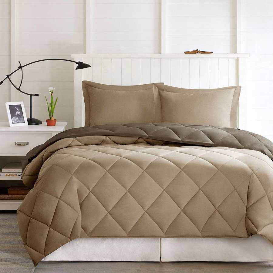 Beige quilted comforter set on a bed in a bedroom setting with a lamp and plant on a nightstand.
