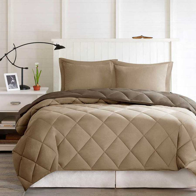 Beige quilted comforter set on a bed in a bedroom setting with a lamp and plant on a nightstand.