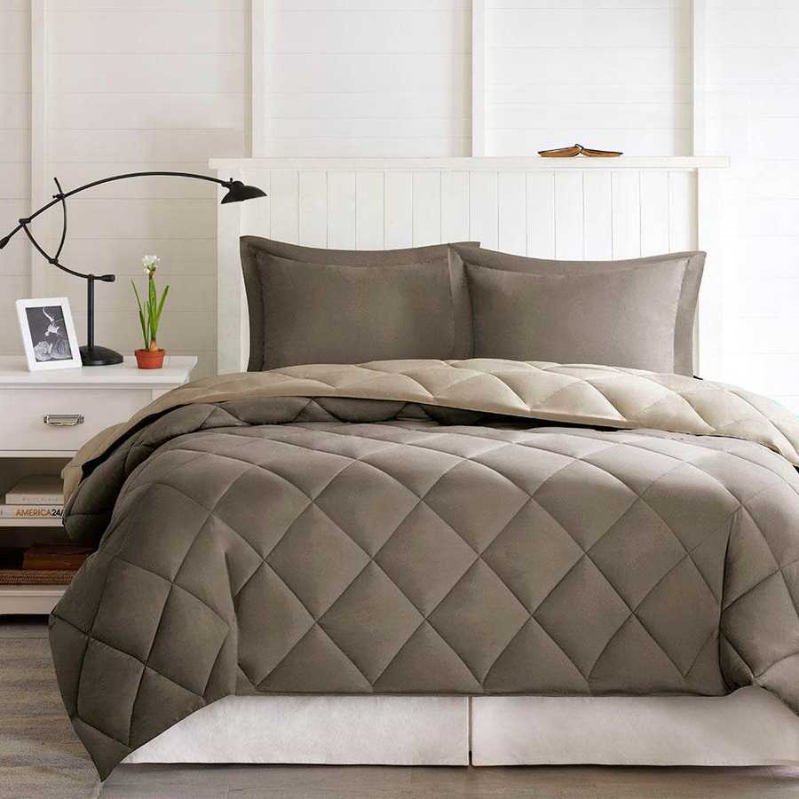 Quilted comforter set on a bed in a bedroom setting with a lamp and plant.