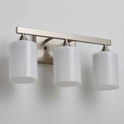 A three-light bathroom vanity wall sconce with a brushed nickel or brass horizontal bar and three white cylindrical frosted glass shades, shown mounted on a light gray wall.