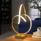 Gold table lamp with circular design on a wooden surface, blurred background of a room.
