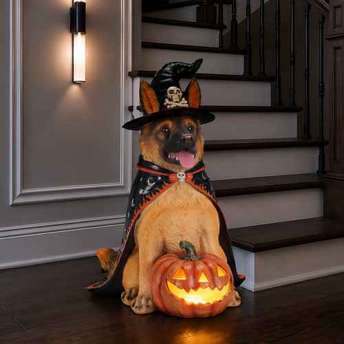 A Halloween dog statue posed sitting on a wooden floor in front of a staircase, wearing a witch hat with a skull detail and a black cape with red trim, with a glowing jack-o&