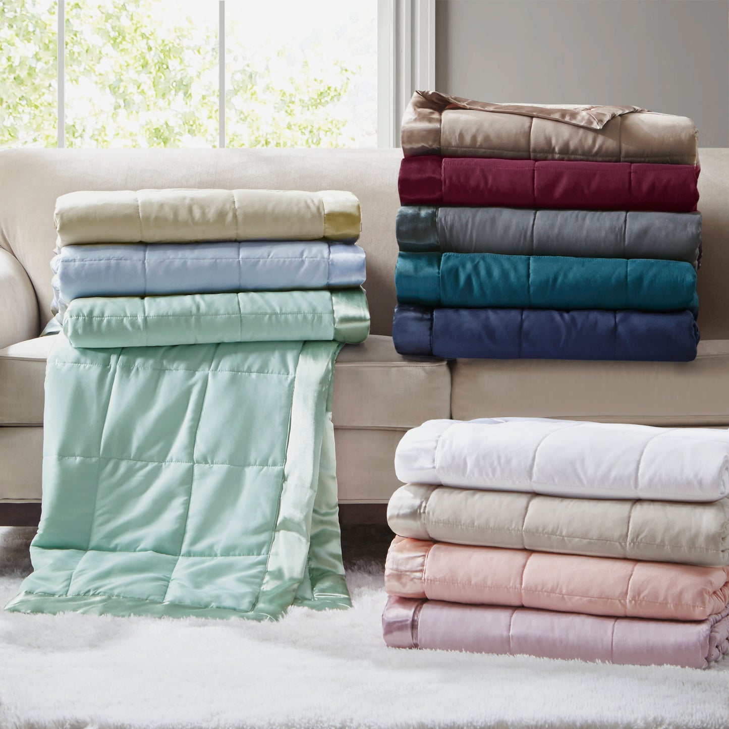 Assorted Down Alternative Blankets with satin trim in various colors neatly stacked on a sofa, showcasing soft, hypoallergenic bedding options.