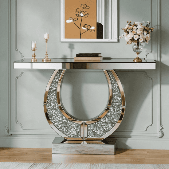 A luxury console table with a mirrored glass top and a large horseshoe-shaped base covered in sparkling silver rhinestones, set against a light sage green paneled wall.