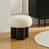 Round ottoman with white cushion and black cylindrical legs in a room setting.