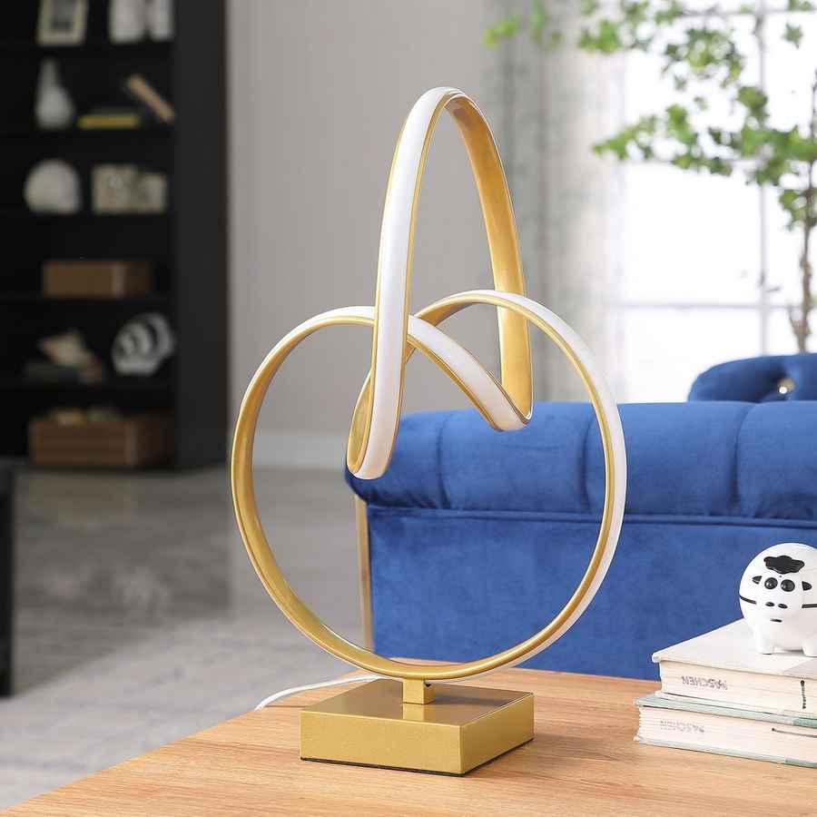 Modern gold table lamp with circular design on a wooden surface in a living room setting.