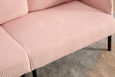 Close-up of a pink ribbed sofa with black legs on a carpeted floor.