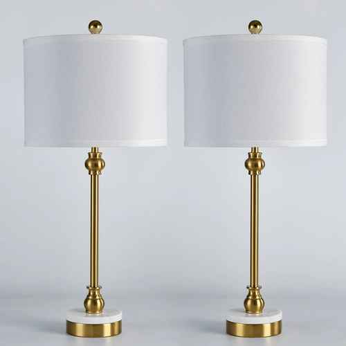 A pair of table lamps with white drum shades, polished gold-finished metal stems and bases, and round white marble-like feet, shown against a light gray studio background.