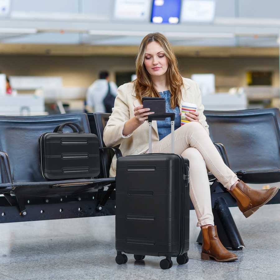 Woman sitting in an airport terminal with a suitcase, using a smartphone.