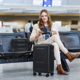 Woman sitting in an airport terminal with a suitcase, using a smartphone.