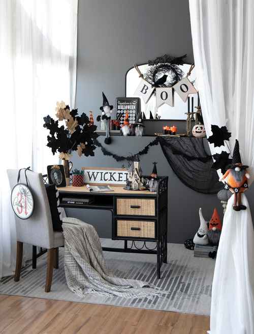 A styled Halloween-themed home office setup featuring a black metal desk with woven drawer fronts, decorated with a &
