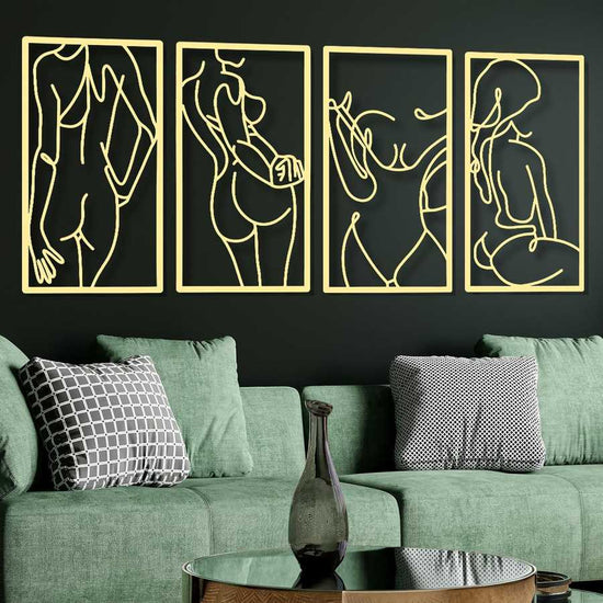Four gold line art wall hangings on a black wall above a green sofa with decorative pillows.