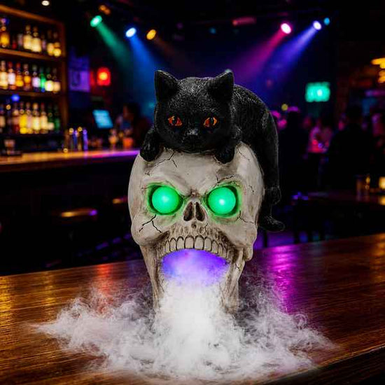 Black cat figurine with orange eyes perched on a skull with glowing green eyes and purple light, Halloween spooky decor