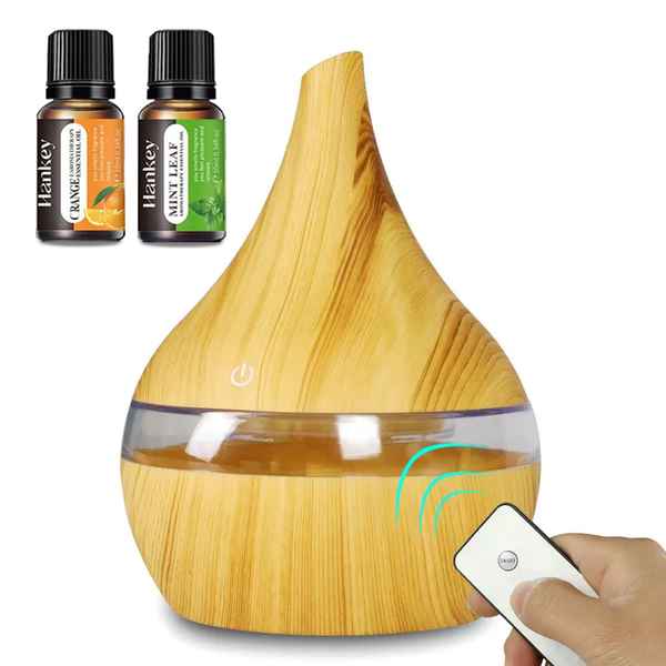 A wooden diffuser with a clear water chamber and a hand holding a white remote, shown on a white background with two small essential oil bottles labeled Leafkey in the upper left.