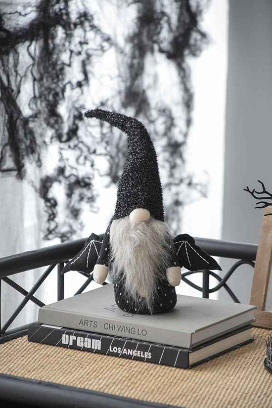 Gnome figurine with a black hat on top of books, with a blurred outdoor background