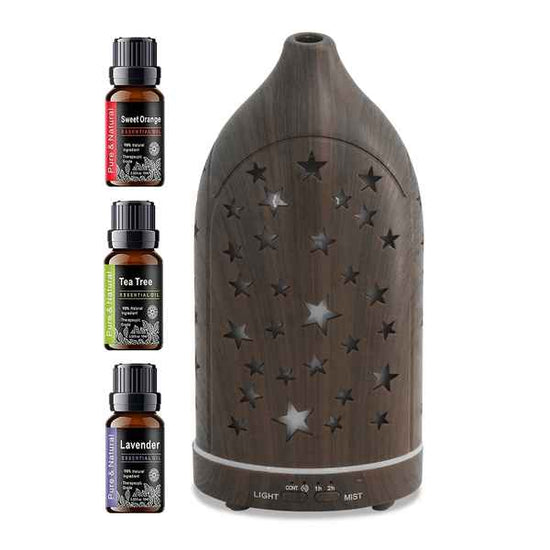 A dark brown wooden diffuser with star-shaped cutouts on the front, shown alongside three small essential oil bottles labeled Sweet Orange, Tea Tree, and Lavender on a white background.