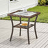 Hexagonal outdoor side table with a glass top and wicker sides on a wooden deck.