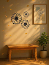 Set of 3 elegant metal sunflower wall art pieces on a sunlit wall above a wooden bench. Ideal for entryway or living room decoration.