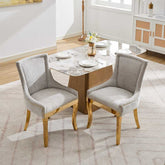 Two gray upholstered chairs with gold legs at a dining table in a room.