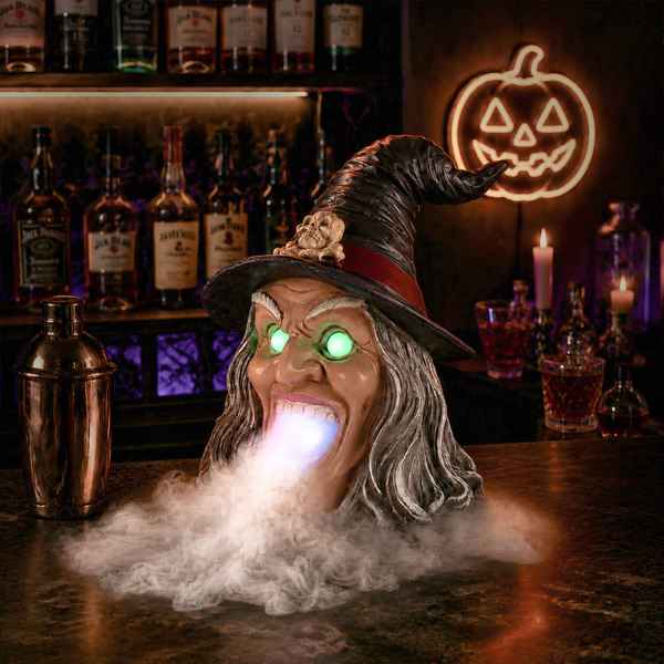 Halloween witch decor with glowing green eyes, wide open mouth, long gray hair, black pointed hat with skull, spooky indoor setting