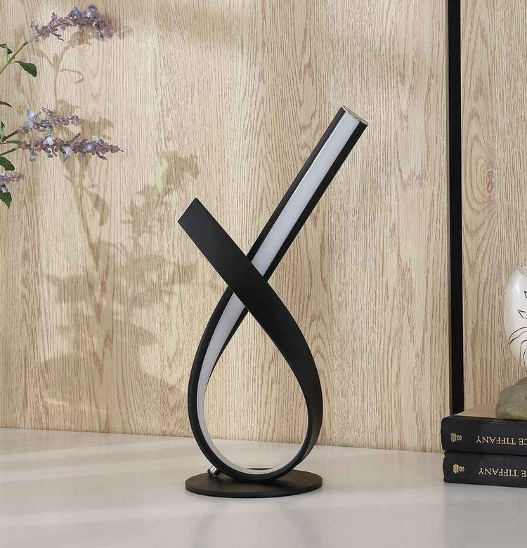 Modern black and white table lamp on a wooden surface with a light wood panel background