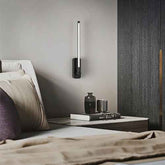 Modern wall-mounted light fixture on a bedroom wall above a nightstand with decorative items.