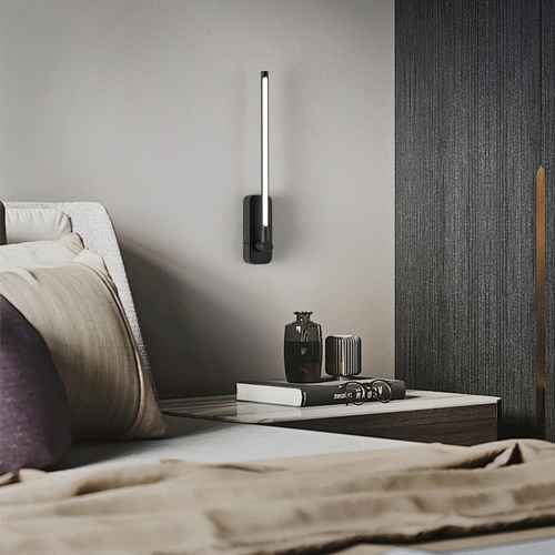 Modern wall-mounted light fixture on a bedroom wall above a nightstand with decorative items.